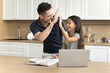 © fizkes - Excited schoolkid girl and happy dad giving high five over learning textbook and laptop on kitchen table, laughing, celebrating education success, achievement, enjoying studying, teaching