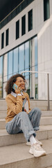 Wall Mural - Cheerful business woman talking phone with client while sitting on stairs on building background