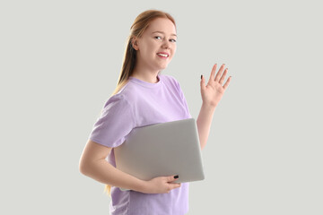 Female programmer with laptop waving hand on light background