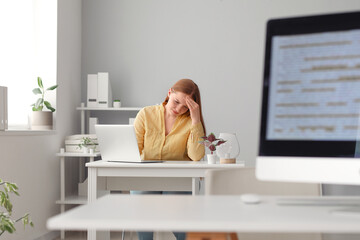 Tired female programmer working with laptop at table in office
