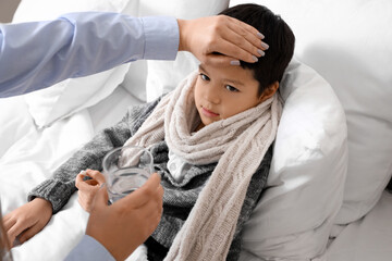 Poster - Ill little Asian boy with pill and his mother touching forehead in bedroom