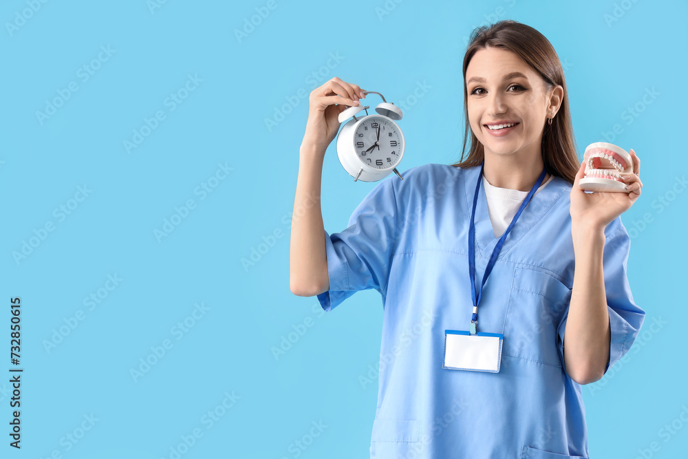 Female dentist with alarm clock and jaw model on blue background