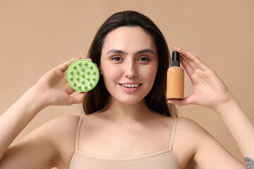 Poster - Beautiful young woman with hair scalp massager and bottle of spray on brown background