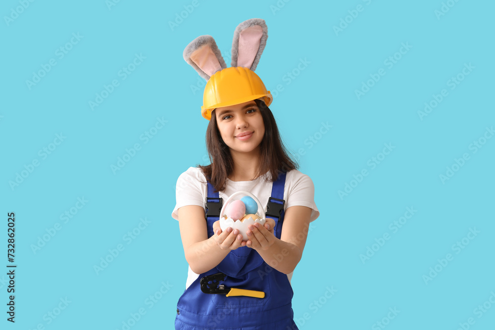 Female worker in bunny ears with Easter eggs on blue background