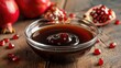 Pomegranate molasses in glass bowl, pomegranate sour sauce with fresh ripe whole and split pomegranate fruit on wooden rustic table