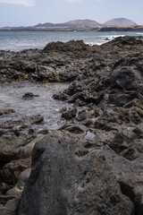 Wall Mural - Seascape. Large white clouds. Mountains in the background. Rocky beach, turquoise Atlantic Ocean. Village of Arrieta. Lanzarote, Canary Islands, Spain