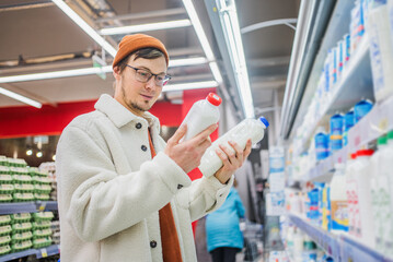 man carefully chooses a bottle of milk in a grocery supermarket. a discerning young man in a stylish