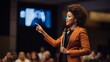 © liliyabatyrova - A beautiful black female motivational speaker makes an inspiring presentation on stage at a business conference in front of a large audience.