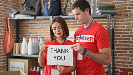Man and woman volunteers standing together holding paper with thank you message at charity center