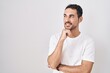 © Krakenimages.com - Handsome hispanic man standing over white background with hand on chin thinking about question, pensive expression. smiling and thoughtful face. doubt concept.