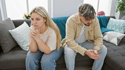 a distressed couple sits apart on a sofa in their living room, embodying tension in their relationsh