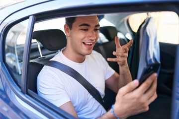 Sticker - Young hispanic man having video call sitting on car at street