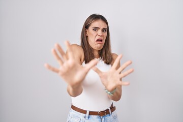 Poster - Hispanic young woman standing over white background afraid and terrified with fear expression stop gesture with hands, shouting in shock. panic concept.