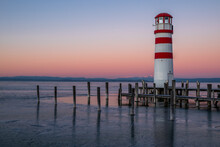 Wooden piles and the frozen Neusiedler See around the striped lighthouse of Podersdorf in Burgenland, Austria during a winter dawn.