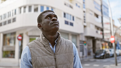 Poster - A contemplative african man standing on a city street with buildings and cars in the background