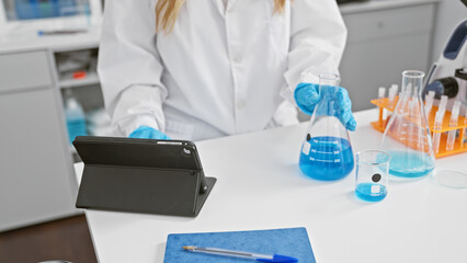 Poster - Serious woman scientist working on medical research in lab, hands measuring liquid in test tube, using touchpad on lab table