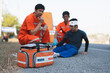 Asian male EMS paramedics or emergency medical technicians in orange uniforms performing first aid to patient with leg injury from road accident