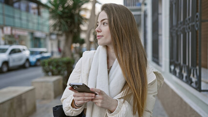 Poster - A thoughtful young woman holding a smartphone stands on an urban street lined with cars and buildings.