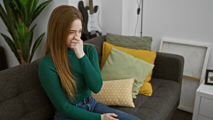 Sticker - Caucasian woman feeling unwell, sitting on a couch at home with a hand covering her nose, in a cozy living room.