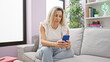 © Krakenimages.com - Young blonde woman using smartphone sitting on sofa with serious face at home