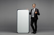 © ViDi Studio - Full body fun adult employee business man corporate lawyer wear formal black suit shirt tie work in office big huge blank screen area mobile cell phone show thumb up isolated on plain grey background.