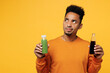 Young man wear casual clothes hold show juice green vegetable smoothie, bottle of soda pop look aside isolated on plain yellow background. Proper nutrition healthy fast food unhealthy choice concept.