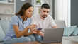 © Krakenimages.com - Beautiful couple in love, sitting together on sofa, engrossed in online shopping using a laptop and credit card, enjoying a relaxed lifestyle within their home's living room interior.