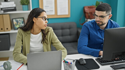 Wall Mural - Two lifestyle professionals, man and woman coworkers, working together using computer and laptop in an elegant office interior