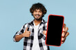 © ViDi Studio - Young Indian man wears shirt white t-shirt casual clothes hold in hand use mobile cell phone with blank screen workspace area show thumb up isolated on plain blue cyan background. Lifestyle concept.
