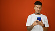 © Krakenimages.com - Cool young tattooed latin man, engrossed in his smartphone over isolated red background, portrait of a serious-looking, concentrated individual immersed in online technology.