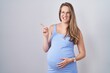 Young pregnant woman standing over white background pointing aside worried and nervous with forefinger, concerned and surprised expression
