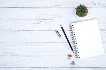 Wall Mural - Blank notepad and with green plant, pen and paper clip on wooden white table desk background ,Top view with copy space, Flat lay