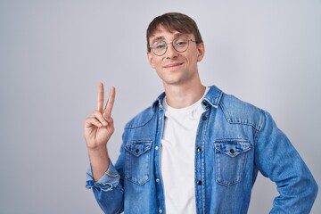 Canvas Print - Caucasian blond man standing wearing glasses smiling looking to the camera showing fingers doing victory sign. number two.