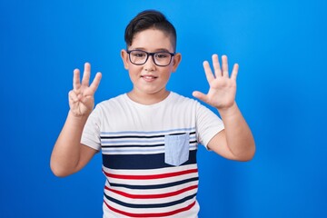 Poster - Young hispanic kid standing over blue background showing and pointing up with fingers number eight while smiling confident and happy.