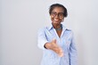 African woman with dreadlocks standing over white background wearing glasses smiling friendly offering handshake as greeting and welcoming. successful business.