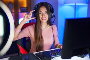 Poster - Young hispanic woman playing video games smiling and confident gesturing with hand doing small size sign with fingers looking and the camera. measure concept.