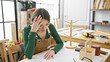 A frustrated woman artisan in a workshop with tools and wooden objects, showing stress at work.