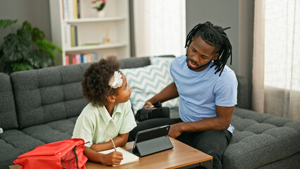 Wall Mural - African american father and daughter sitting on sofa studying at home