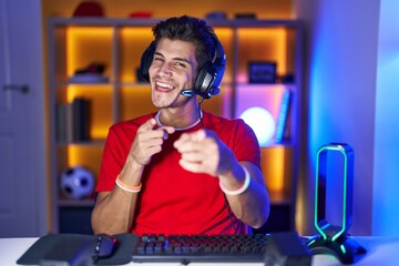 Wall Mural - Young hispanic man playing video games pointing fingers to camera with happy and funny face. good energy and vibes.