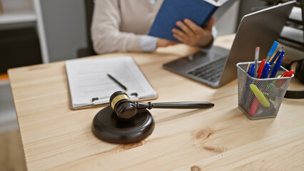 Mature woman lawyer works indoors at office with laptop, gavel, and legal documents on wooden desk.