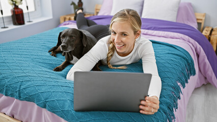 Canvas Print - A young woman and her labrador relax on a bed in a cozy bedroom while working on a laptop.