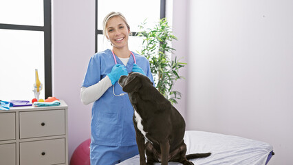 Wall Mural - A smiling young woman veterinarian in scrubs examines a labrador in a well-equipped veterinary clinic.