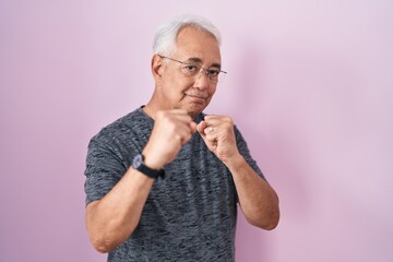 Wall Mural - Middle age man with grey hair standing over pink background ready to fight with fist defense gesture, angry and upset face, afraid of problem