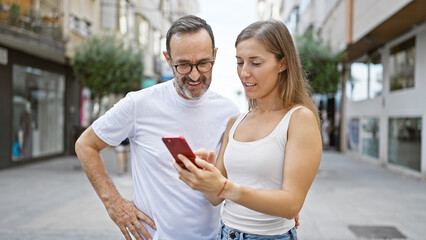 Poster - Cool and confident father smiling with daughter in their casual style, enjoying fun time together using smartphone on lively city street