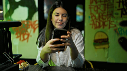 Canvas Print - Young beautiful hispanic woman using smartphone sitting on the table at the restaurant