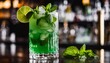 A minty green cocktail with a lime wedge and a sprig of mint