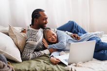 Positive young diverse couple looking at laptop while relaxing on bed