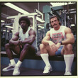  two guys in the 1980s are sit flat bench in the gym, their attire reflecting the fashion of the era. Captured with a Polaroid 600, the photo exudes a nostalgic and retro vibe. 