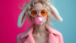 A fashionable young woman with bunny ears blowing a bubble gum bubble, in a stylish pink jacket on teal background. Happy Easter concept
