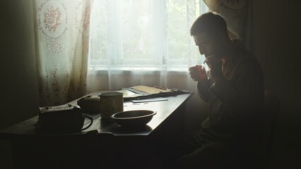 Poster - Adult soldier lighting cigarette in rural house. Side view of male scout in soldier uniform sitting at table in rural house and lighting cigarette with matches